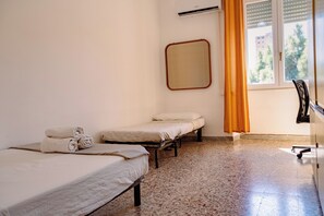 Ein Hotelzimmer mit zwei Einzelbetten, einem kleinen Tisch, einem Sessel, einem Spiegel und einem Fenster mit Vorhängen.