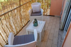Ein Balkon mit Korbmöbeln, einem Glastisch und einem Blumentopf.