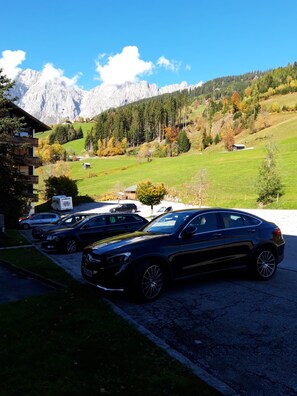 A parking area with a mountain backdrop, a building with a balcony, and a clear sky. - Cozy vacation rental at Alpendomizil—a great ski resort in the Hochkönig region of Austria (Mühlbach am Hochkönig)