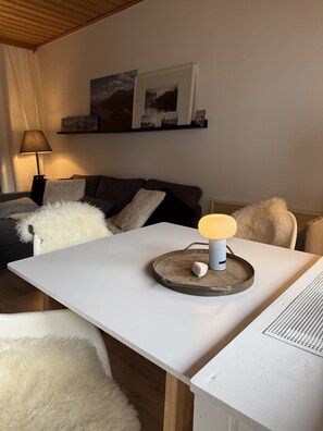 Ein weißer Tisch mit einer Lampe und einer Schale mit einem Stein. Davor steht ein flauschiger, weißer Sessel.