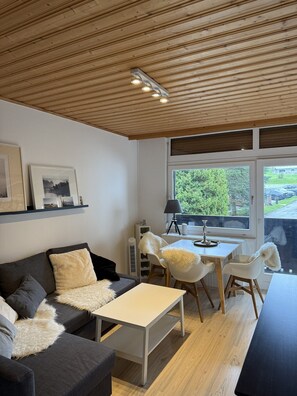 Un salon moderne avec un plafond en bois, un canapé doté de coussins moelleux, une table basse blanche et un coin repas avec une table et des chaises.