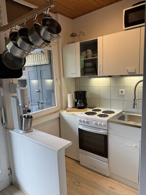 Une cuisine de taille réduite avec des meubles blancs, une cuisinière, un évier et des casseroles suspendues.