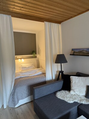 Ein Schlafzimmer mit einem Bett, einem Sofa, einer Lampe und einem Fenster mit Vorhängen.