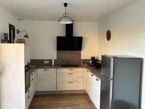 A modern kitchen with a built-in oven, a microwave, and a refrigerator. - Across the Fields (Duttlenheim)
