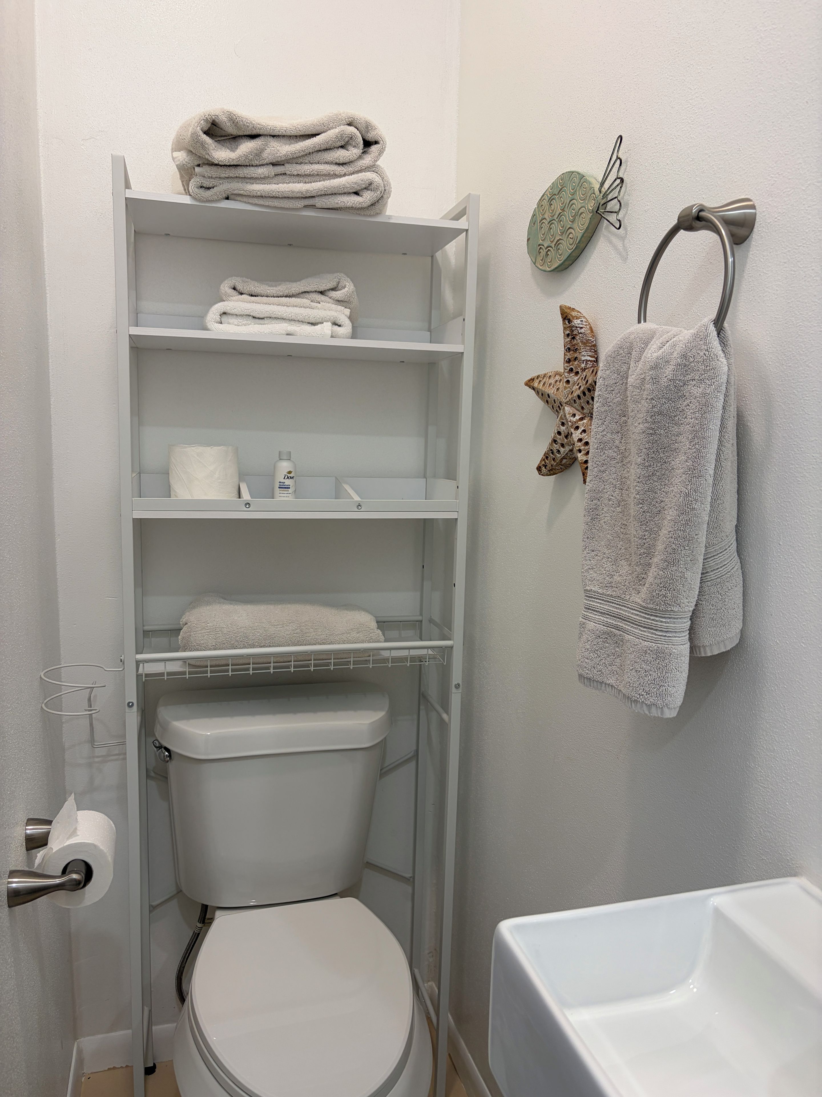 A bathroom with a toilet, a shelf with folded towels, a toilet paper holder, and a towel rack with a towel.