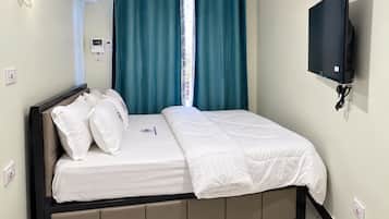 Una habitación de hotel con cama, cortinas, televisor montado en la pared y termostato.