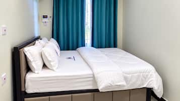 Una cama bien hecha con cubrecama blanco y almohadas, un cabecero con panel de control, cortinas color turquesa y piso de mármol.