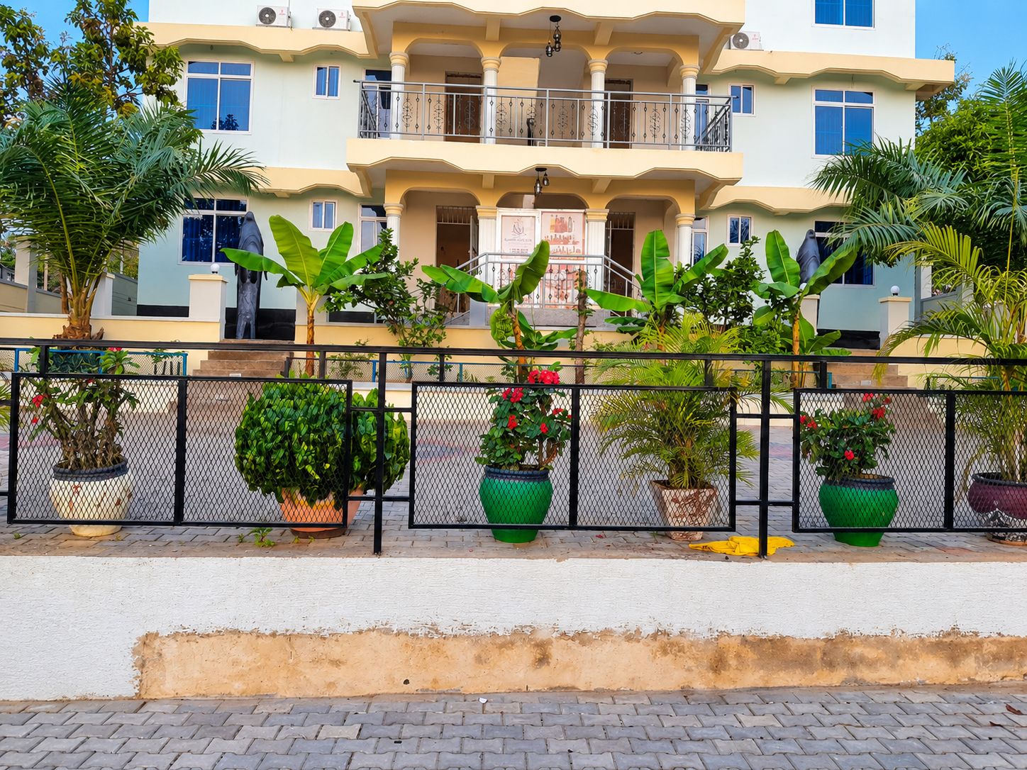 Un edificio de varios pisos con balcones, plantas en macetas y un paseo pavimentado.
