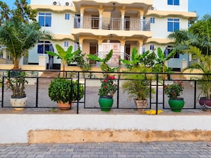 Um edifício de vários andares com varandas, plantas em vasos e um calçada pavimentada.