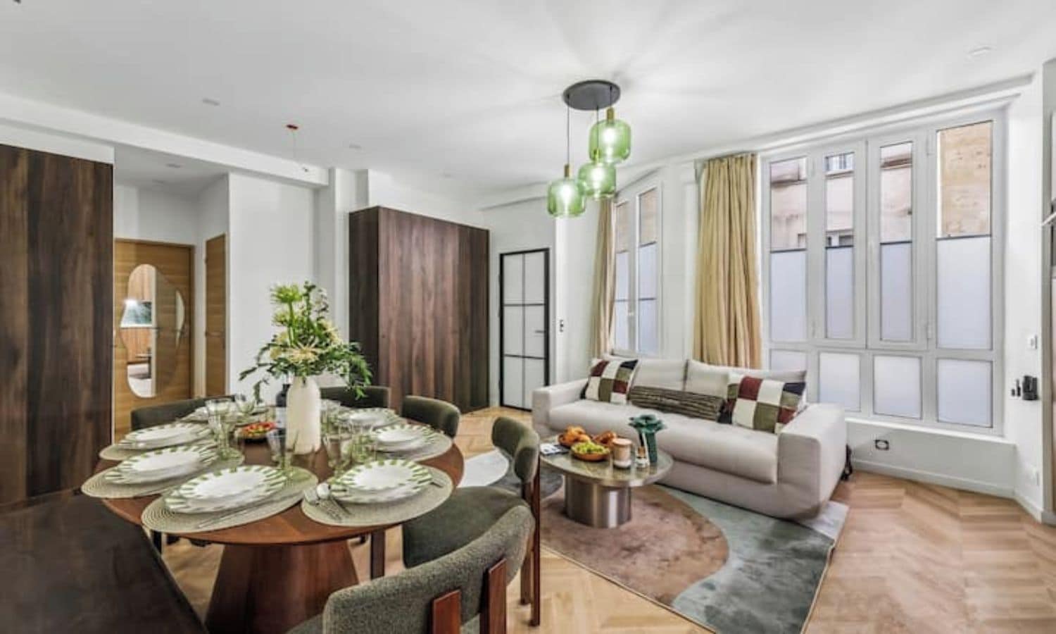 A modern living room with a dining area, large windows, and a sofa with cushions.