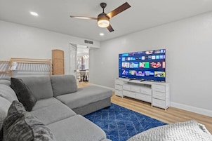 A modern living room with a sectional sofa, a flat-screen TV, and a ceiling fan.