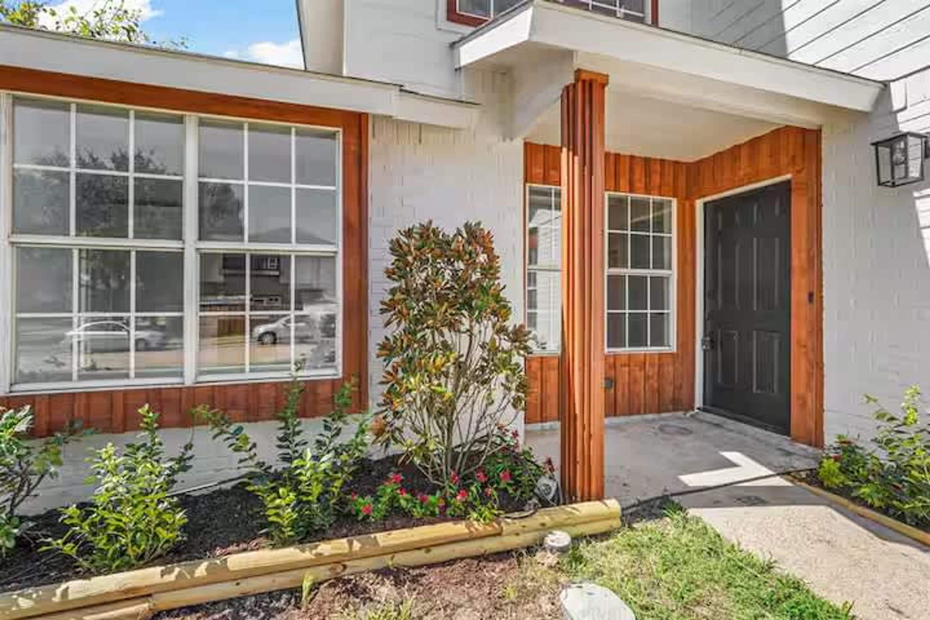 A modern house with large windows, a wooden front door, and a well-maintained garden.