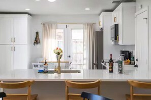 Eine moderne Küche mit weißen Schränken, einer zentralen Kochinsel mit Barhocker, einem Kühlschrank und einer Mikrowelle.
