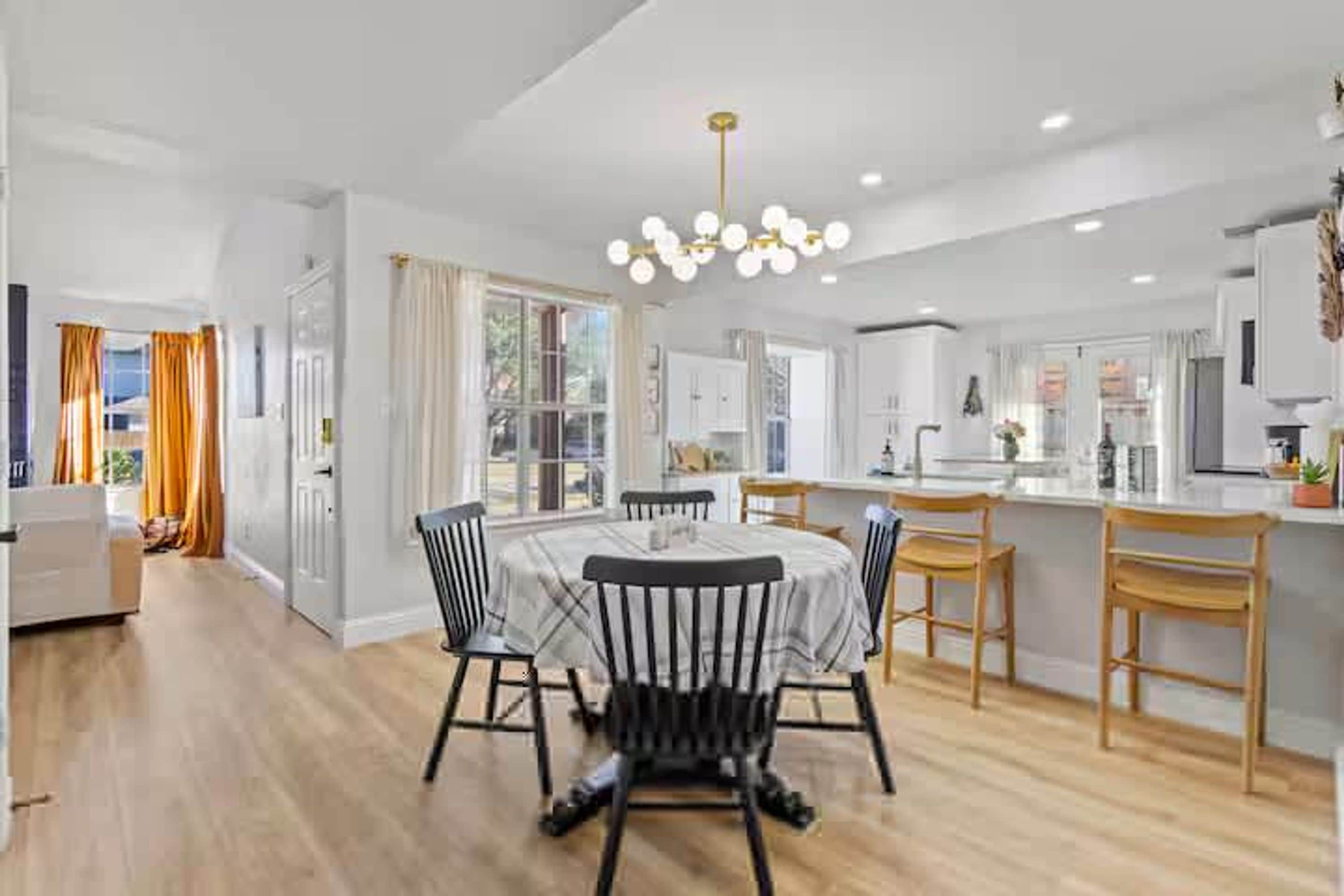 A modern kitchen with white cabinets, a central island, and a dining area with a round table and chairs.