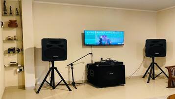 A living room with a television mounted on the wall, two speakers on stands, a DJ mixer, and a shelf with decorative items.