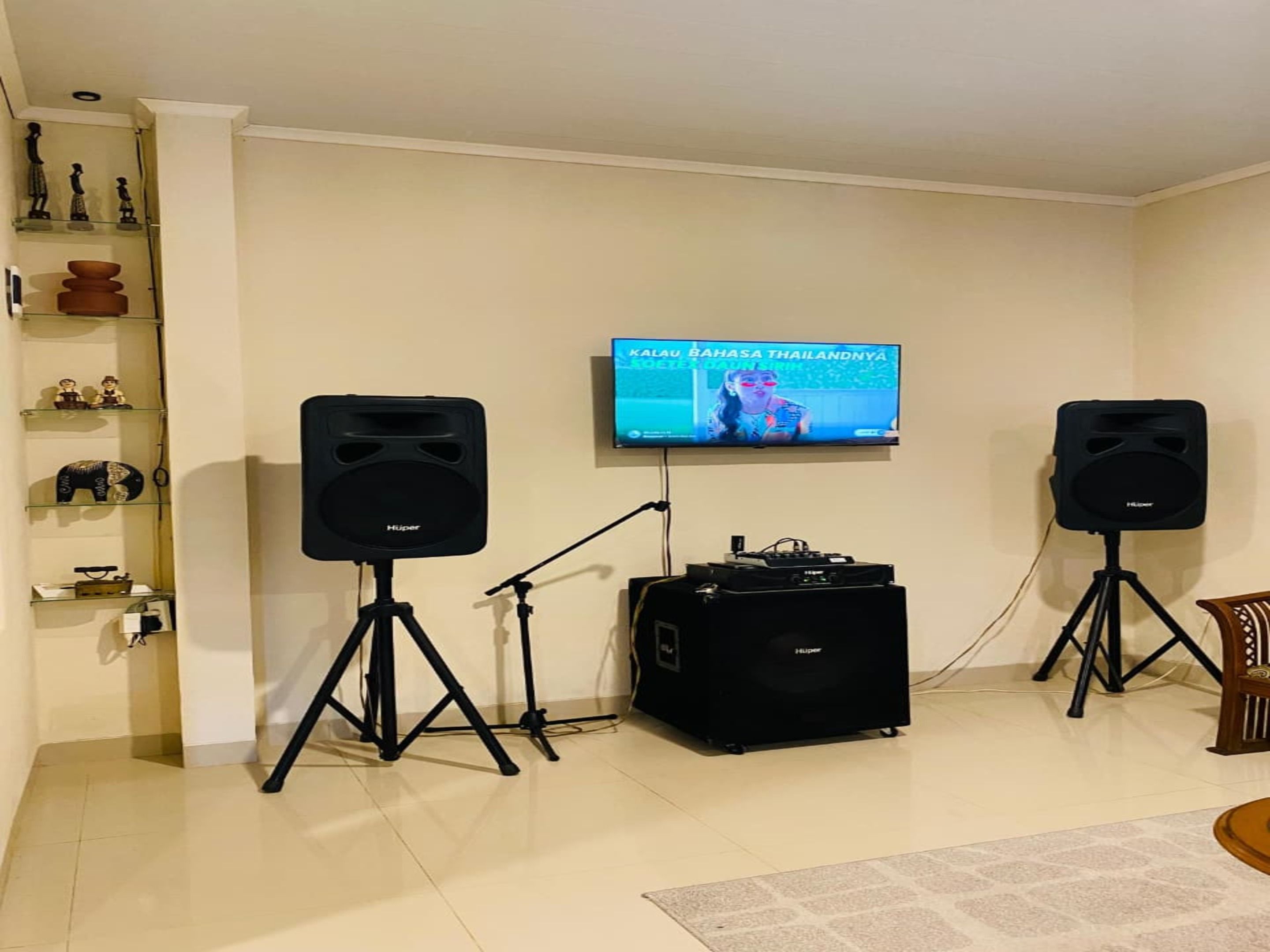 Un saló amb televisió penjada a la paret, dos altaparlants sobre pedestals, un mezclador de DJ i una estanteria amb objectes decoratius.
