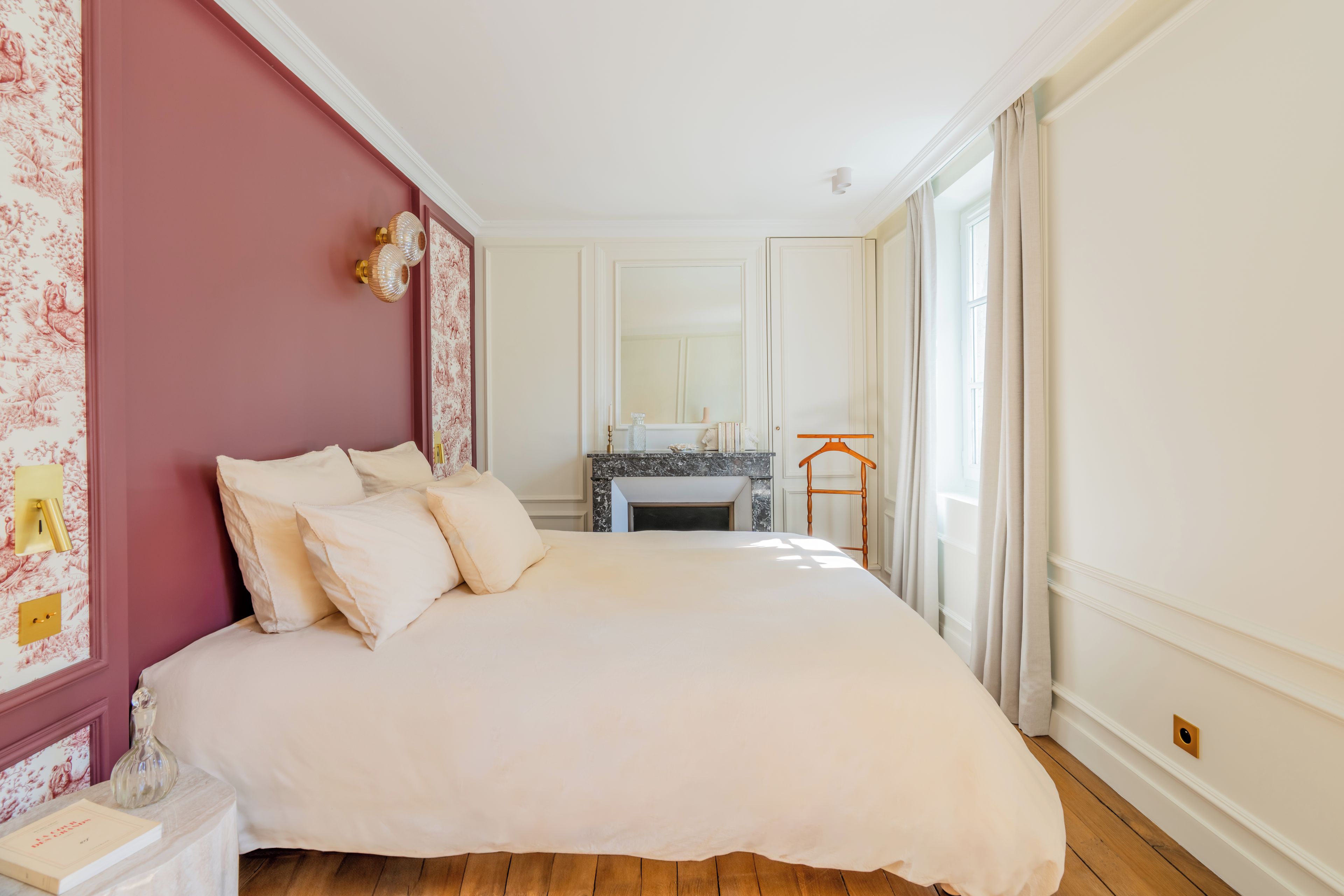A bedroom with a large bed, a nightstand, a dresser, a mirror, and a window with curtains.
