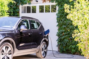 Ein schwarzer SUV steht draußen, verbunden mit einem Ladekabel an einer Ladestation.