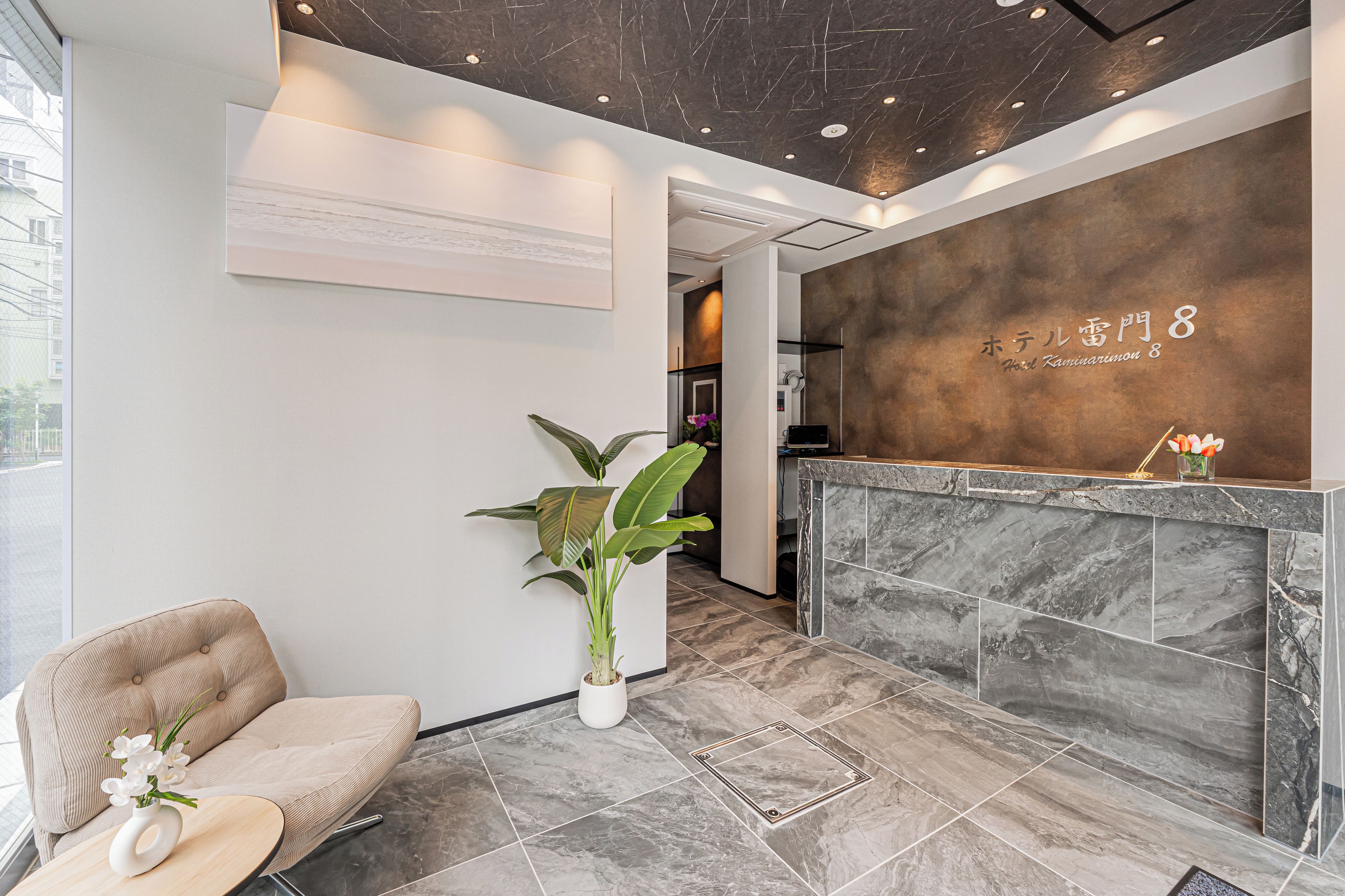 A reception area with a marble reception desk, a seating area with a sofa and a potted plant, and a wall-mounted sign.