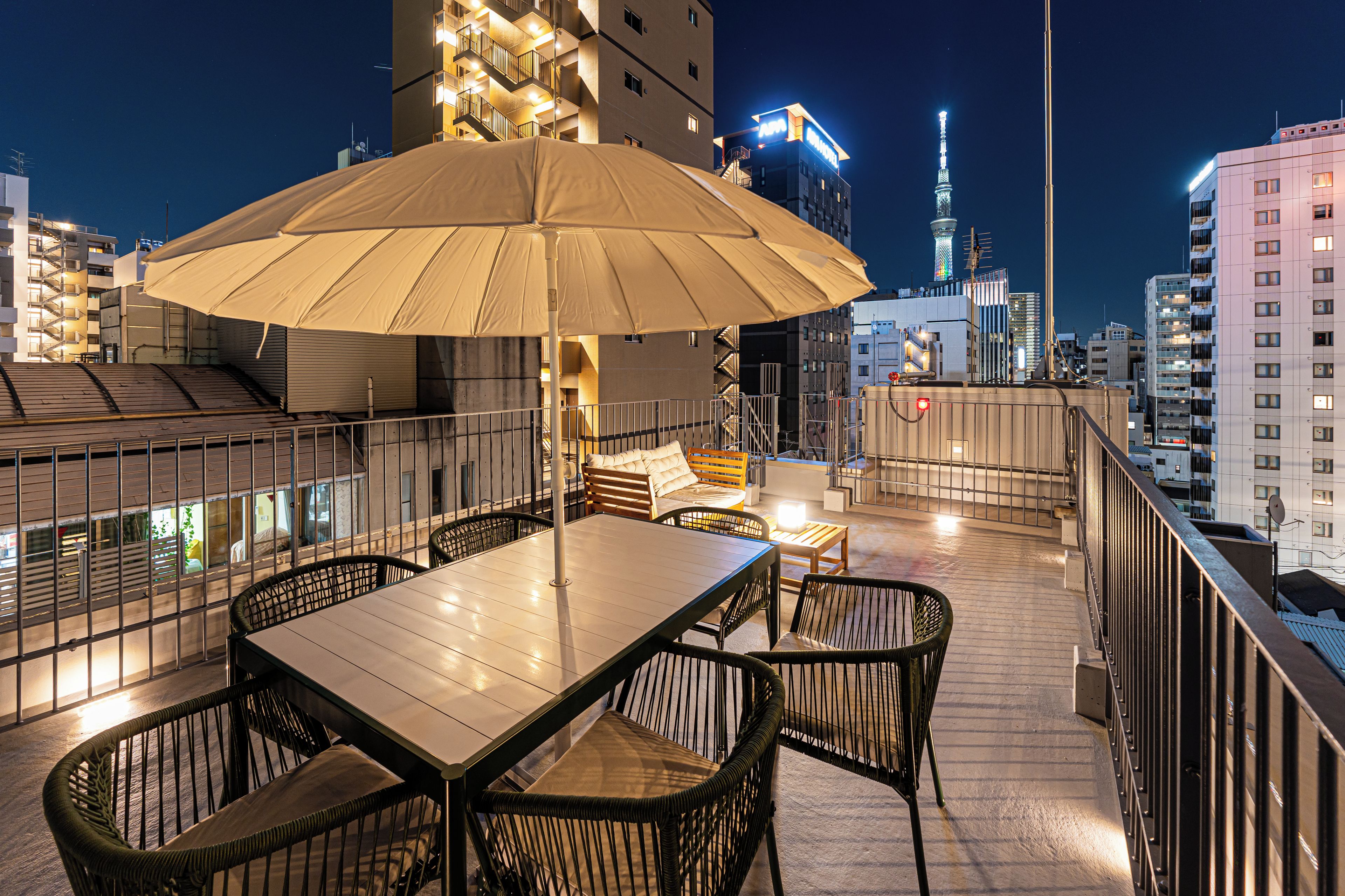 An outdoor terrace with a table and chairs, a large umbrella, and a cityscape view in the background.