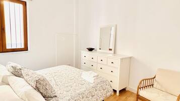 Un dormitorio con cama, cómoda, silla y lámpara colgante.