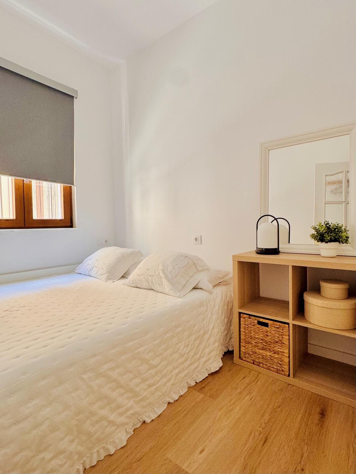 Un dormitorio con cama, mesita de noche, espejo y ventana.