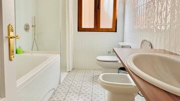 Un baño con bañera, inodoro, bidé y un espejo grande.