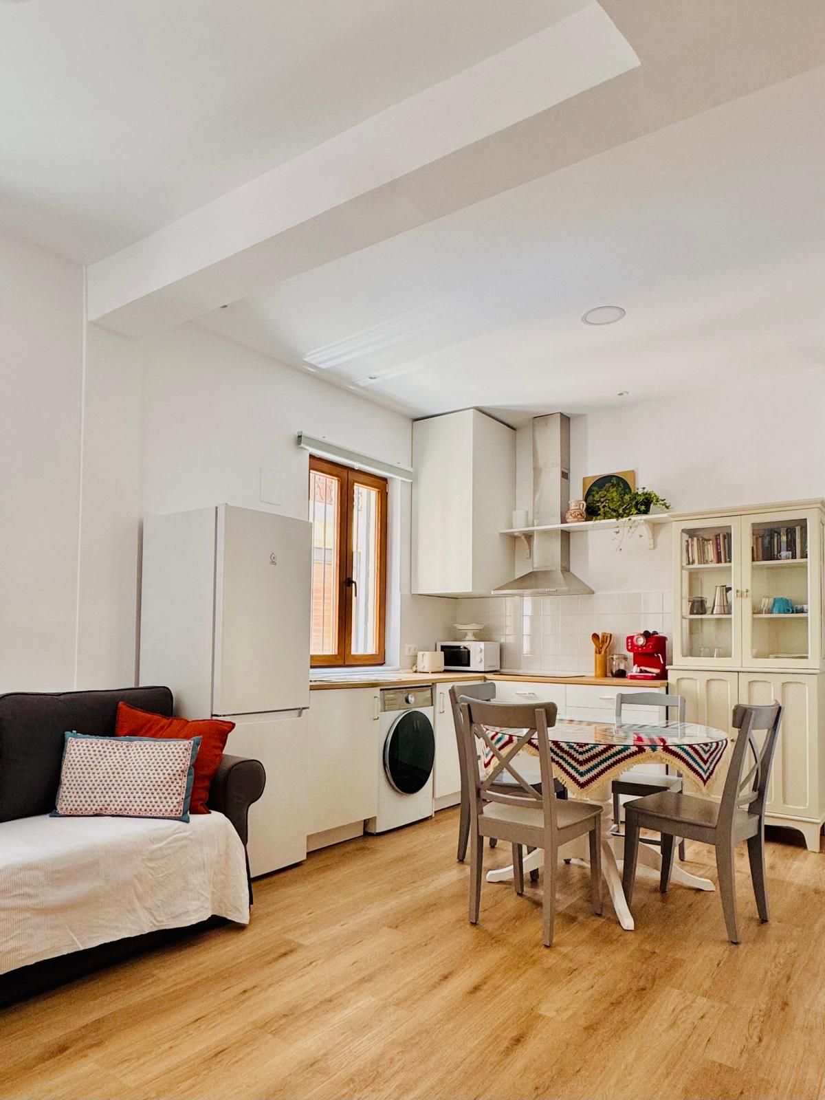 A compact living space with a kitchenette, a dining area with a table and chairs, and a sofa with cushions.
