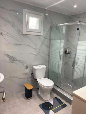 A bathroom with a toilet, a glass shower enclosure, a small stool, and a window. - Brand new House with Veranda for family 2 minutes from the sea (Agia Triada)