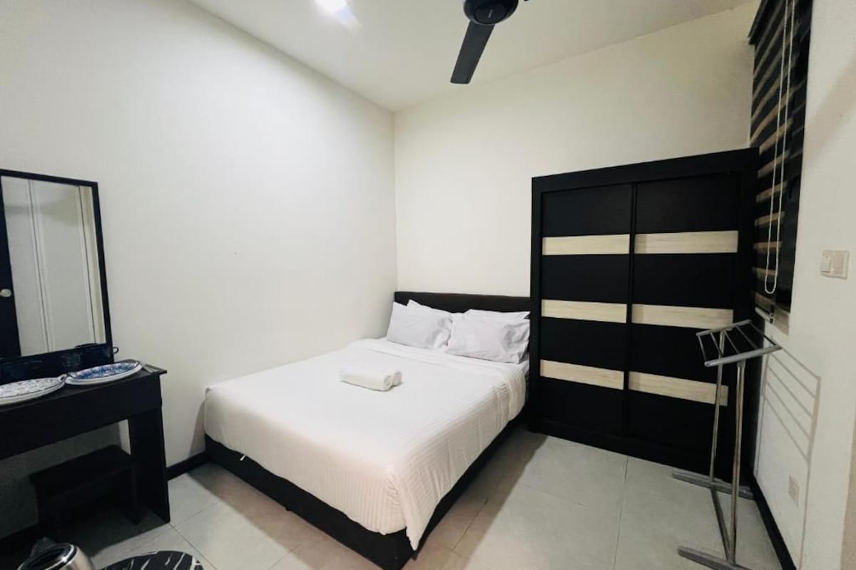 A bedroom with a bed, a desk, a mirror, and a ceiling fan.