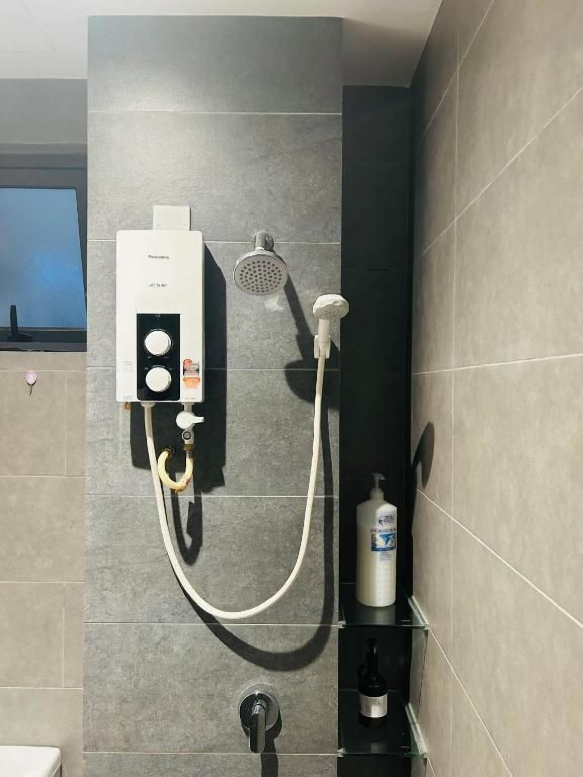 Un baño con ducha, cabezal de ducha de mano y una botella de champú en un estante.
