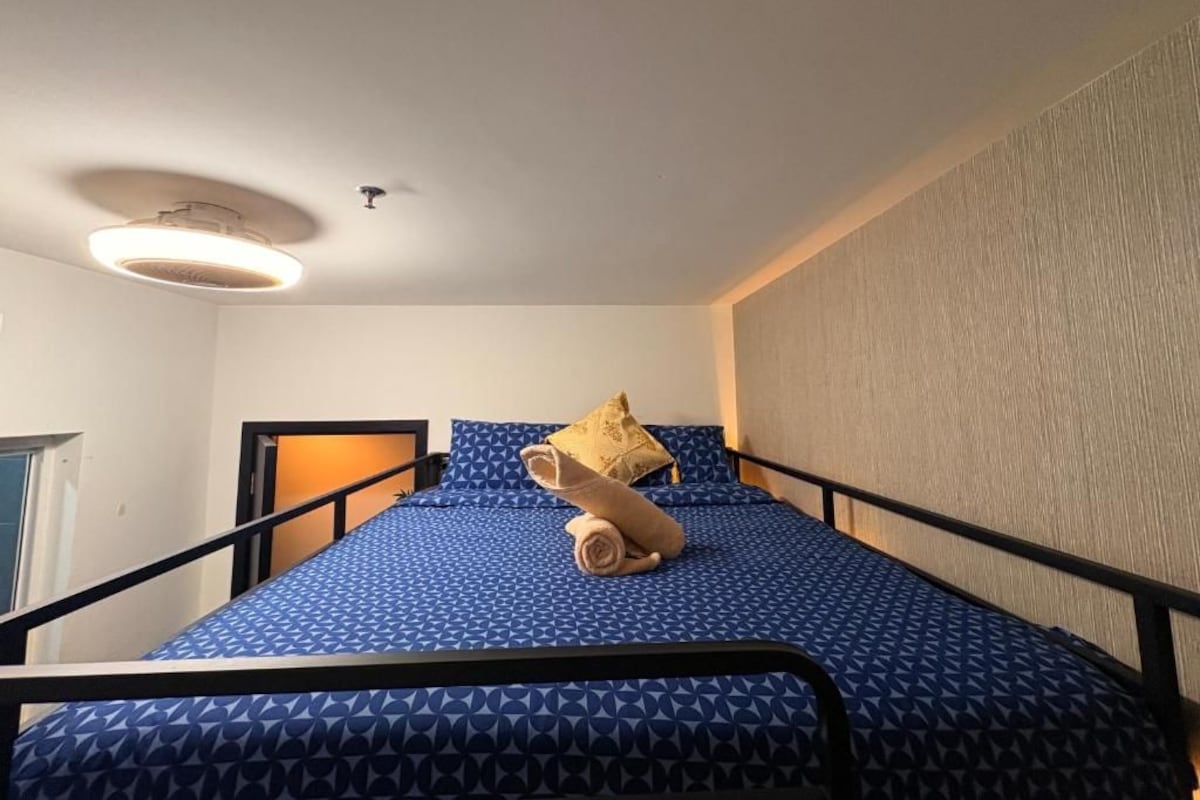 A single bed with a patterned blue mattress, a headboard, and a wall-mounted light fixture.