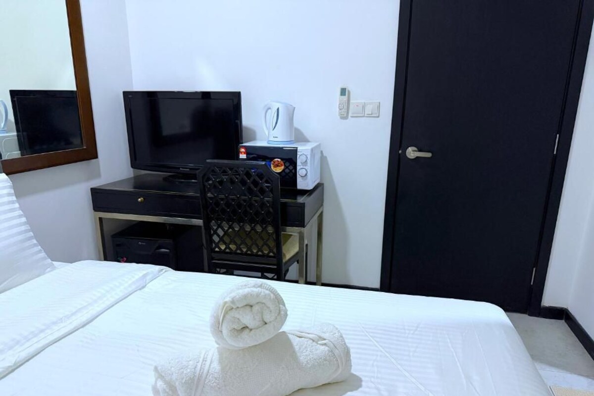 A hotel room with a bed, a desk with a television, a microwave, and a door.