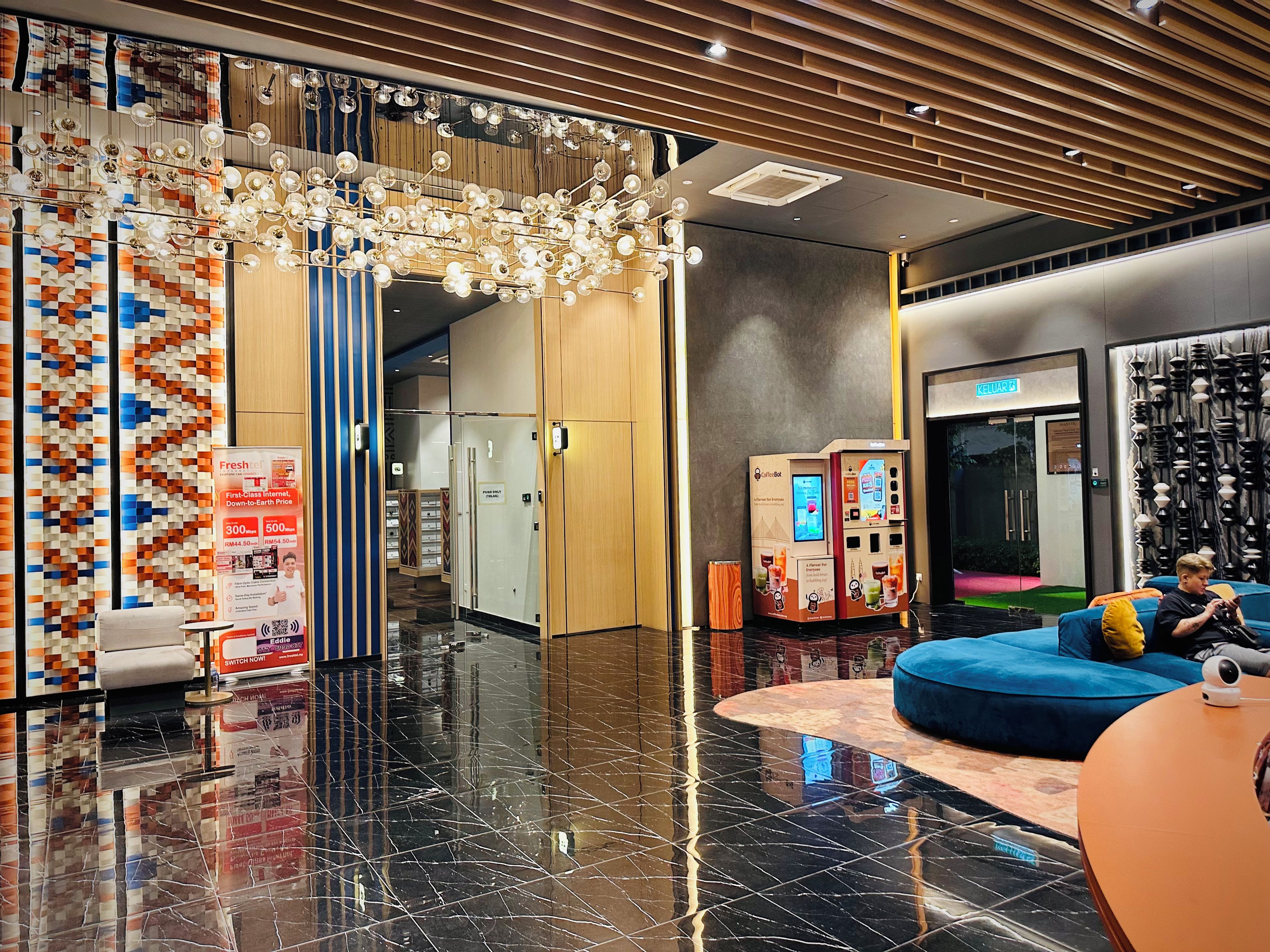 A modern lobby with a marble floor, a seating area with a blue sofa, a coffee machine, and a wall with patterned curtains.