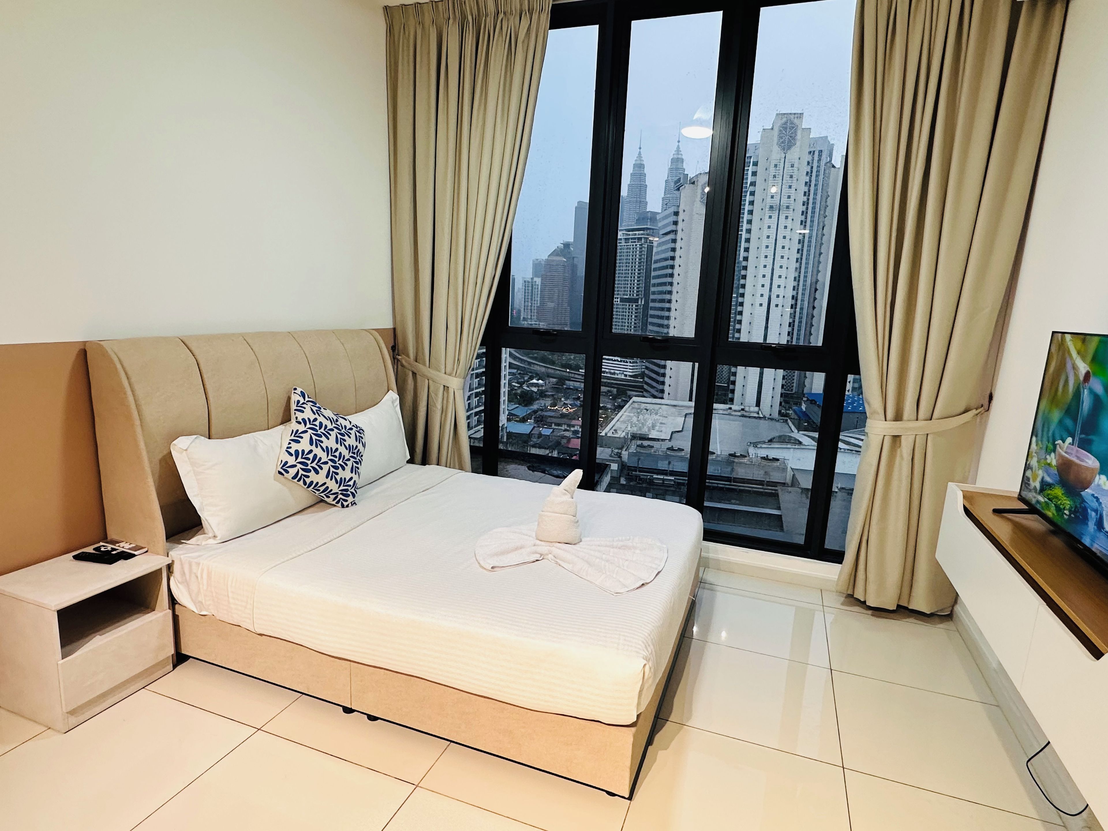 A hotel room with a bed, a nightstand, a TV, and a large window with a city view.