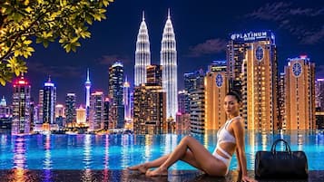 Una mujer sentada junto a una piscina, con el horizonte de la ciudad al fondo, incluyendo las Torres Petronas.