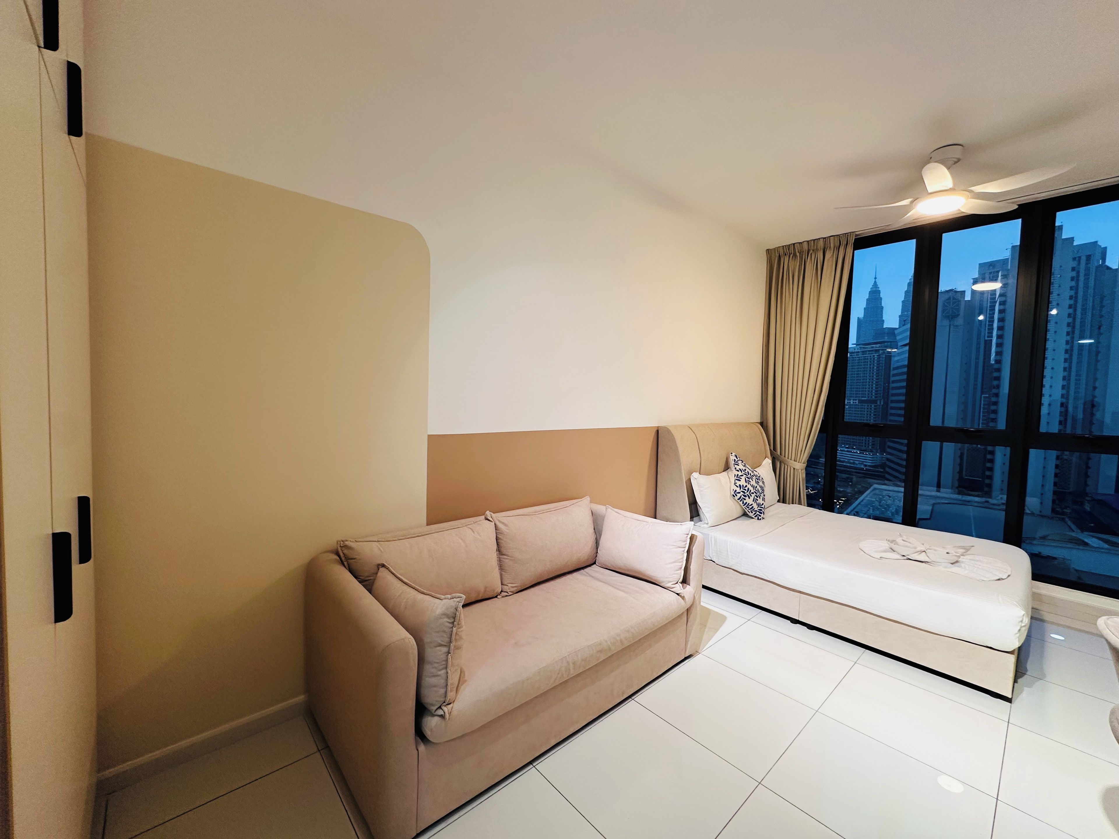 Una habitación de hotel moderna con un ventanal grande, un sofá, una cama y un ventilador de techo.