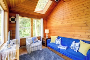 Ein gemütliches Blockhaushaus-Interieur mit einem blauen Sofa, einem gestreiften Sessel, einem kleinen Tisch mit Lampe und einem Fernseher.