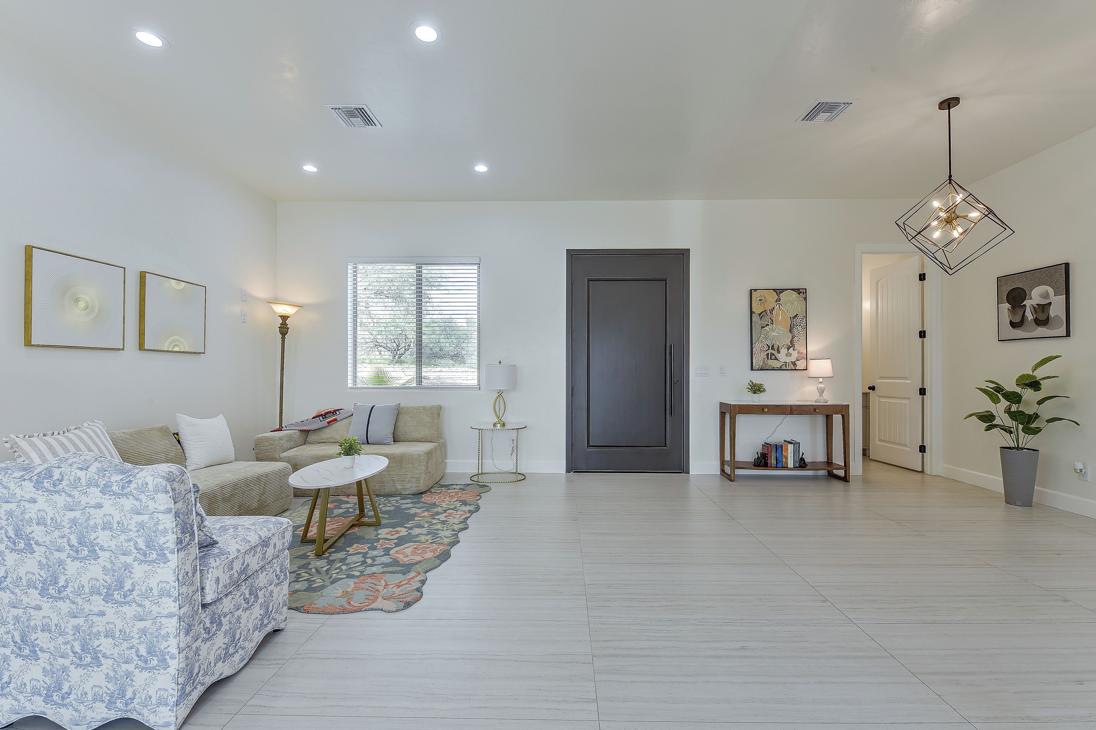 A spacious living room with a sofa, a coffee table, and a rug. There is a door leading to another room and a window with blinds.