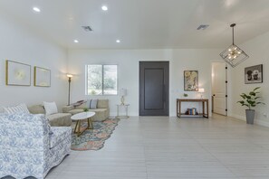 A spacious living room with a sofa, a coffee table, and a rug. There is a door leading to another room and a window with blinds. - Modern Rio Rico Home Near Nogales & Lake Rec! (Rio Rico)
