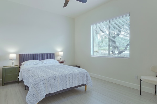 A bedroom with a bed, nightstands, a window with blinds, and a chair.