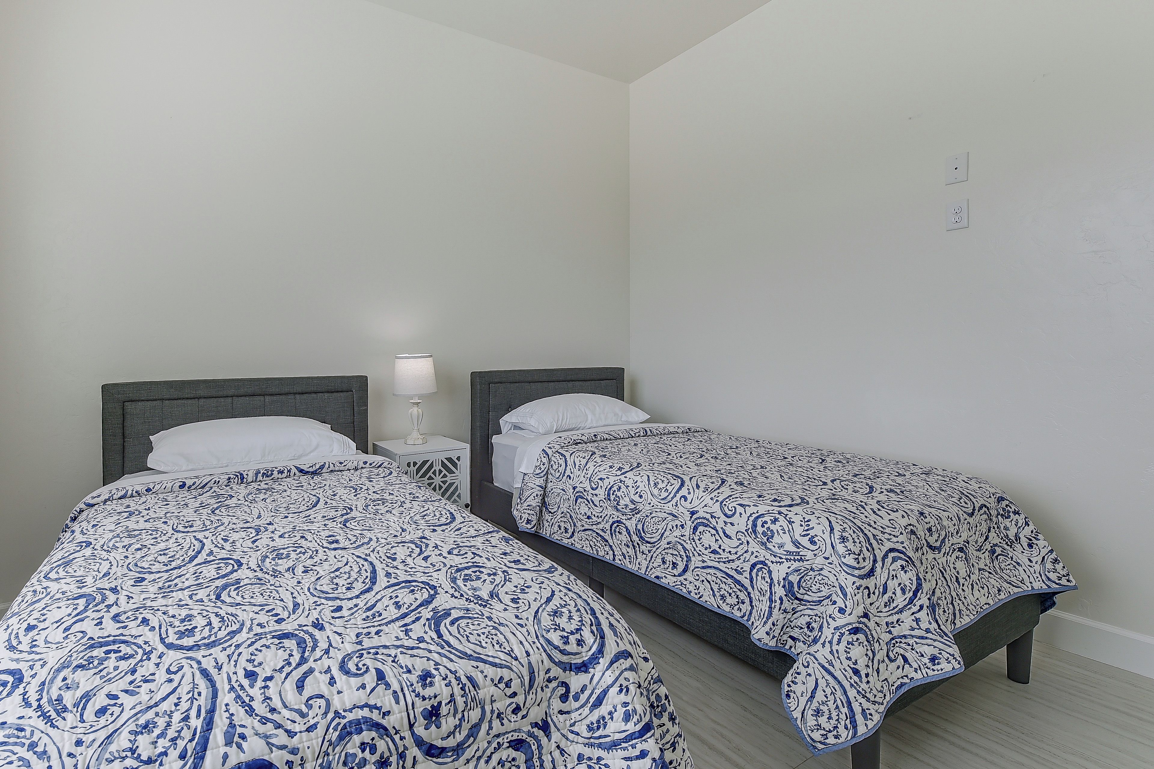 A room with two single beds, each with a headboard, a bedside table, and a lamp.