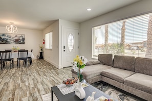 A modern living room with a sofa, a dining area with chairs, and a large window with blinds. - Desert Oasis: Home Near Joshua Tree NP! (Twentynine Palms)