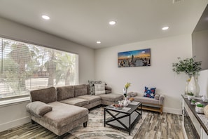 A modern living room with a sectional sofa, a coffee table, and a cityscape painting. - Desert Oasis: Home Near Joshua Tree NP! (Twentynine Palms)