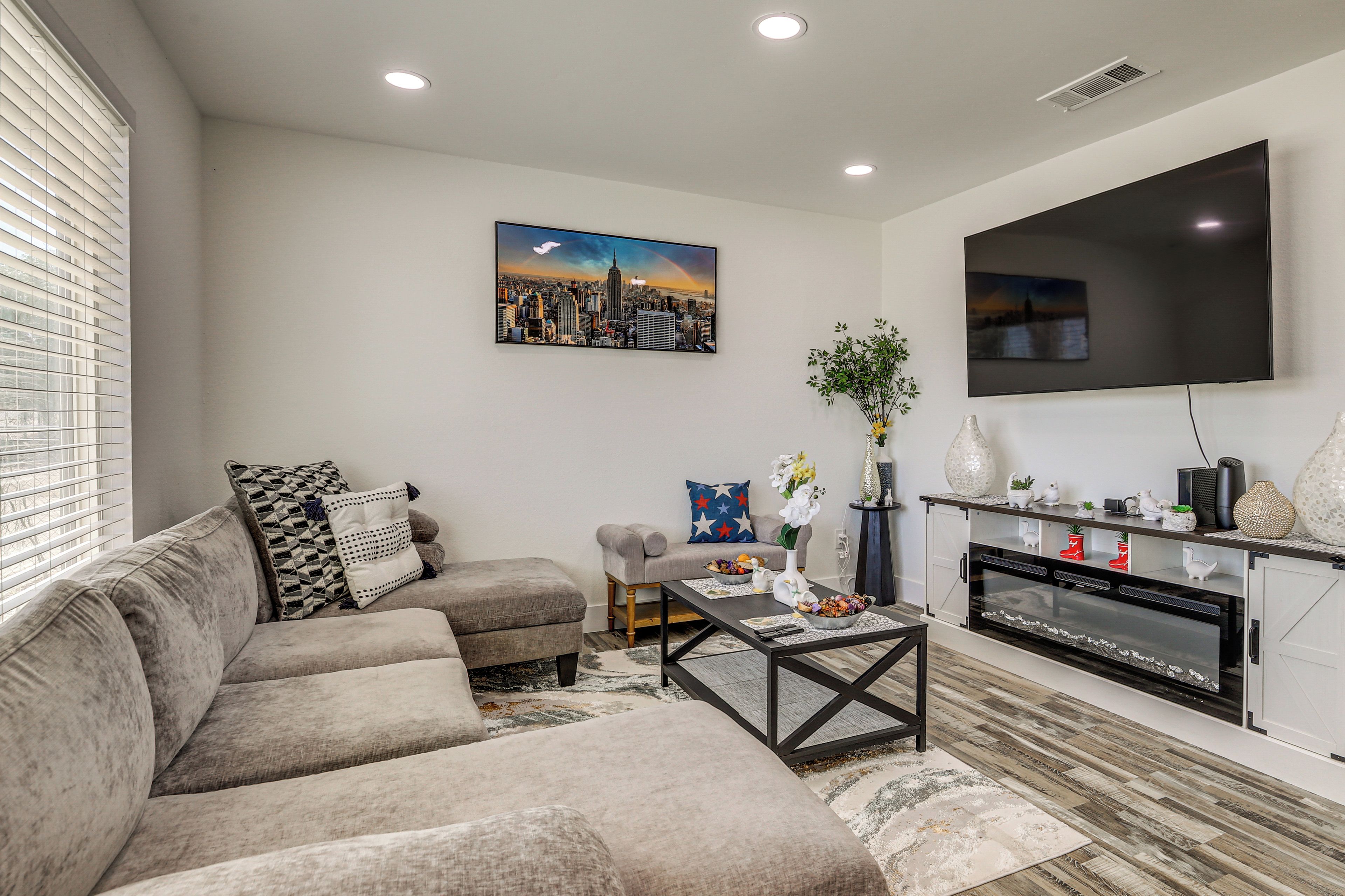 A modern living room with a sectional sofa, a flat-screen TV, and a cityscape painting.