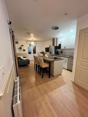 A modern kitchen with a central island, a dining area with a sofa, and a hallway leading to another room. - 3-Bedroom Apartment · 33 m² South-Facing Terrace · Les Halles, 4 min away (Pau)