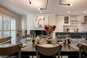 A modern dining room with a table set for four, a vase with dried flowers, and a kitchen in the background. - Home Away From Holmes - Cosy 3 Bedroom Marylebone (London)