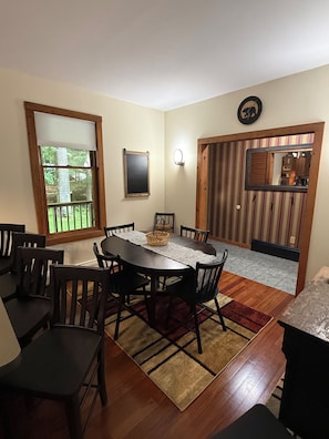 A dining area with a round table, chairs, a wooden floor, a window with blinds, a wall-mounted clock, and a striped wall. - Serene 5-bedroom house in delightful Old Forge perfect for families (Old Forge)