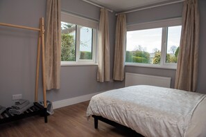 A bedroom with a bed, two windows, a radiator, a wooden ladder, and a wall socket. - entire 3 bed home on the outskirts of Donegal Town (Donegal Town)