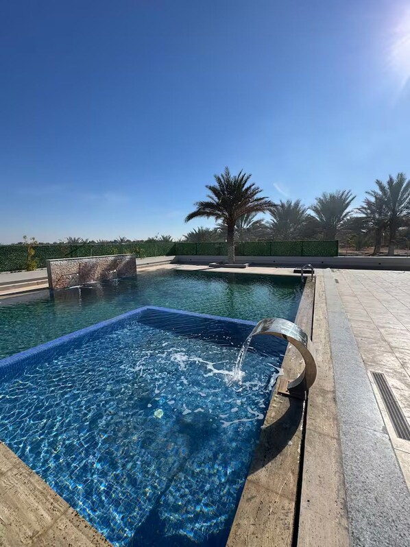 Una piscina con agua cristalina, rodeada de un solado de baldosas y palmeras.